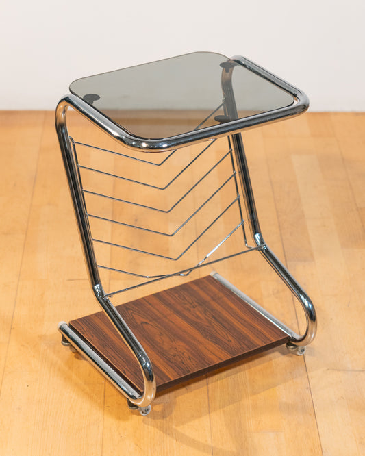 1970s chrome rolling side table with smoked glass top, wooden shelf, wheels, and magazine rack. Vecino Shop