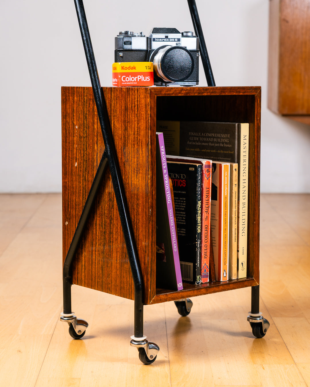 Vintage 1950s mid-century modern rolling side table, wood veneer, tubular black metal frame, chrome wheels, built-in bookcase. Vecino Shop
