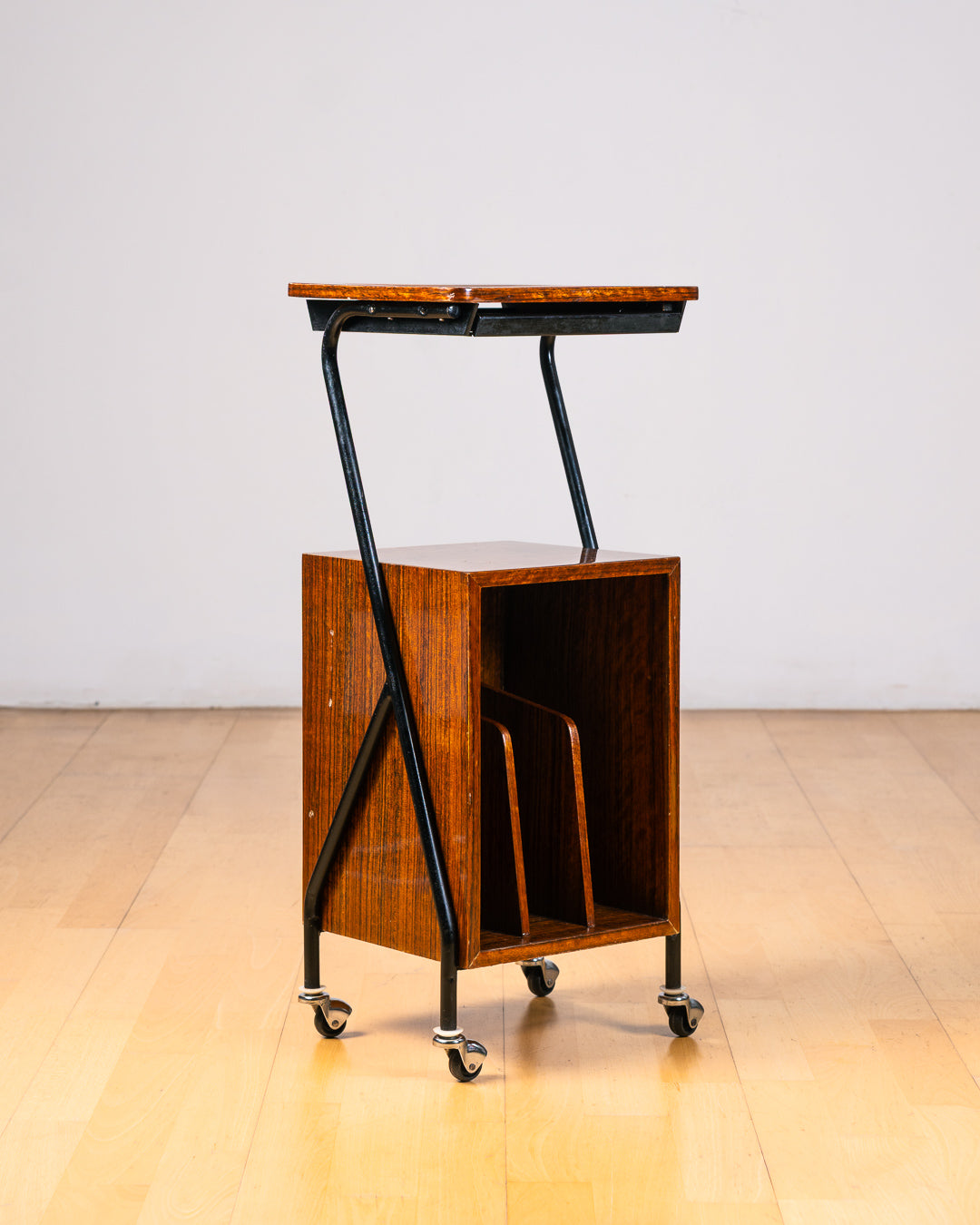 Vintage 1950s mid-century modern rolling side table, wood veneer, tubular black metal frame, chrome wheels, built-in bookcase. Vecino Shop