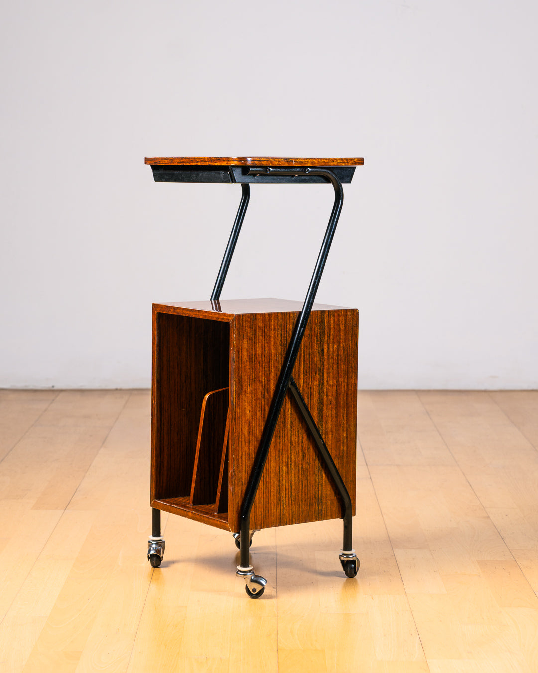 Vintage 1950s mid-century modern rolling side table, wood veneer, tubular black metal frame, chrome wheels, built-in bookcase. Vecino Shop
