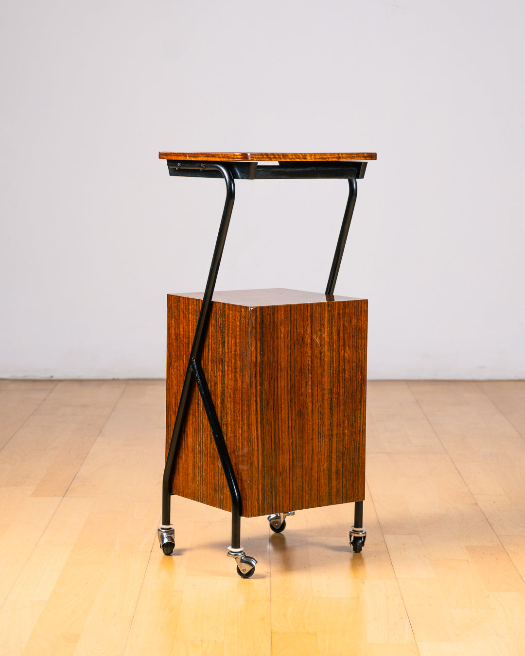Vintage 1950s mid-century modern rolling side table, wood veneer, tubular black metal frame, chrome wheels, built-in bookcase. Vecino Shop