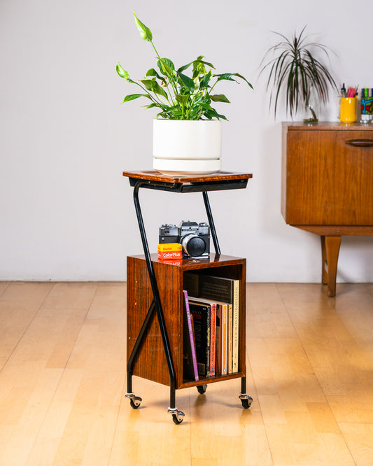 Vintage 1950s mid-century modern rolling side table, wood veneer, tubular black metal frame, chrome wheels, built-in bookcase. Vecino Shop