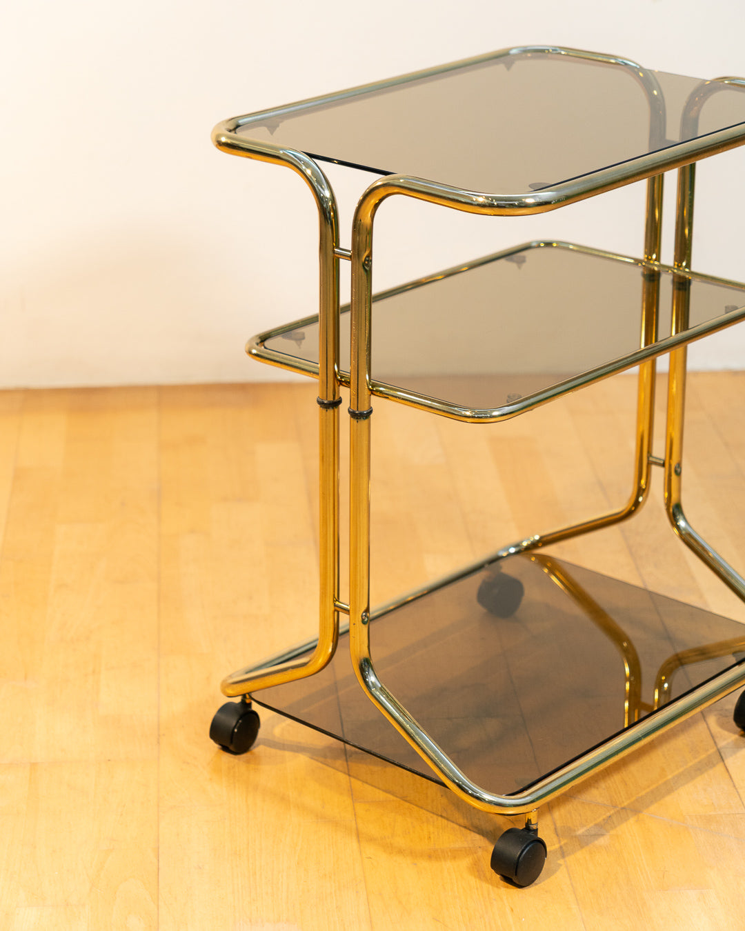 Rare 1970s tubular gold rolling side table with three smoked glass tiers and wheels, vintage Space Age design. Vecino Shop