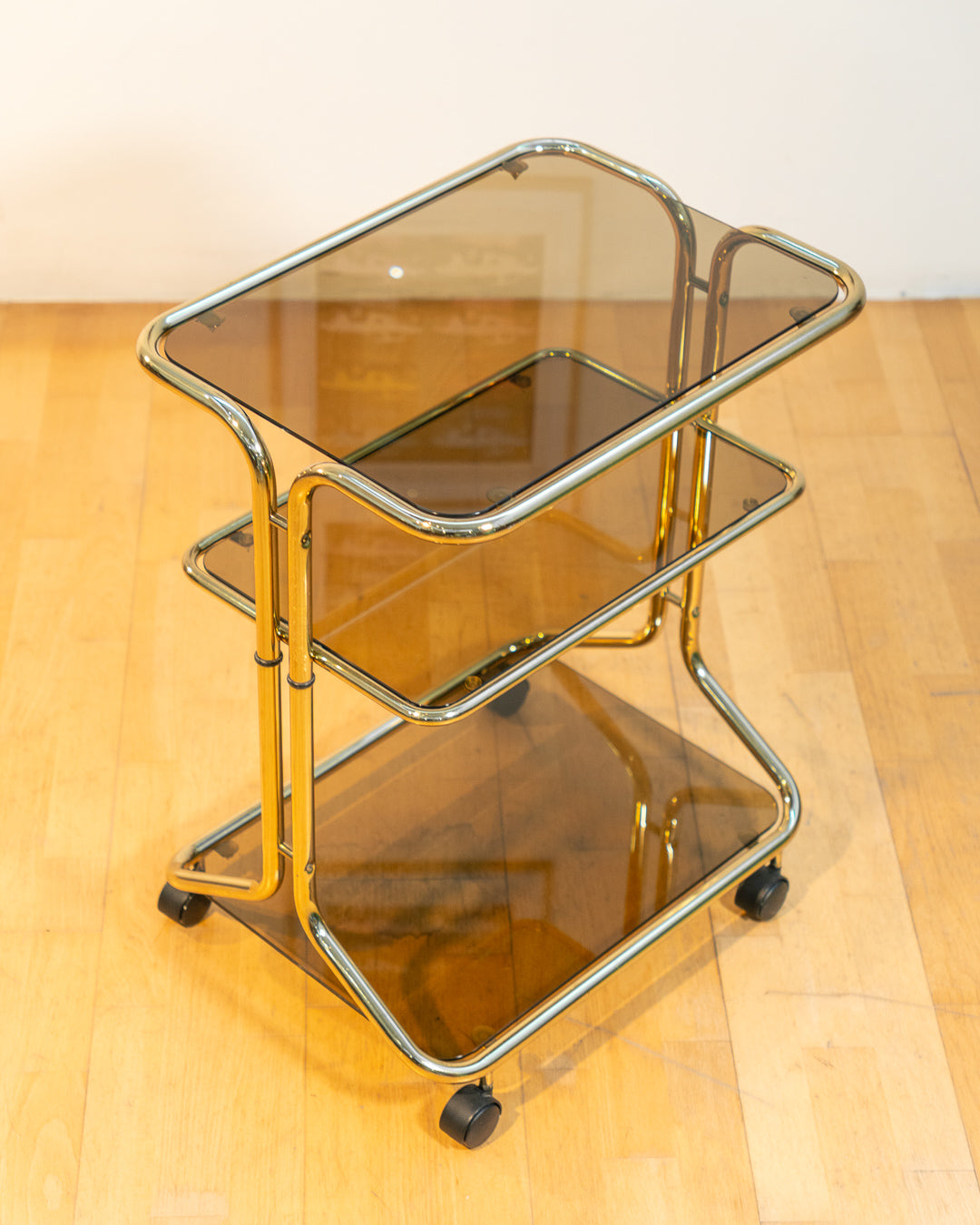 Rare 1970s tubular gold rolling side table with three smoked glass tiers and wheels, vintage Space Age design. Vecino Shop