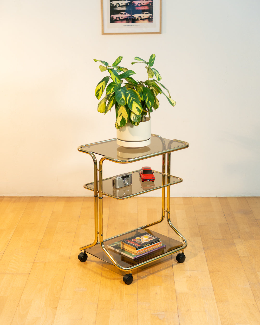 Rare 1970s tubular gold rolling side table with three smoked glass tiers and wheels, vintage Space Age design. Vecino Shop
