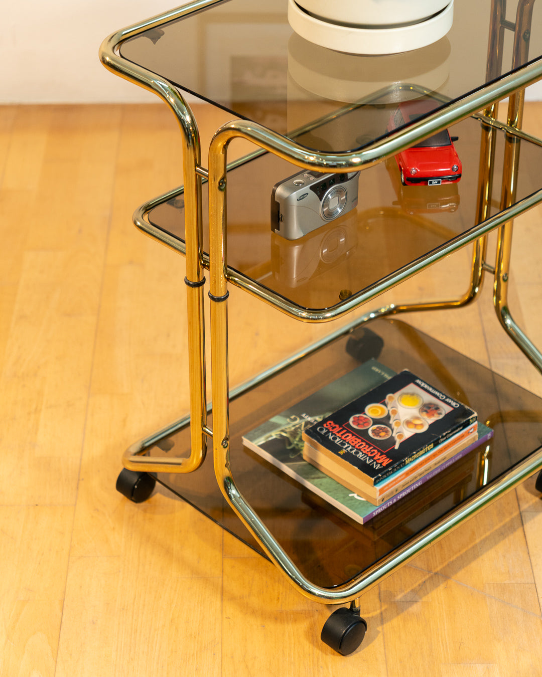 Rare 1970s tubular gold rolling side table with three smoked glass tiers and wheels, vintage Space Age design. Vecino Shop