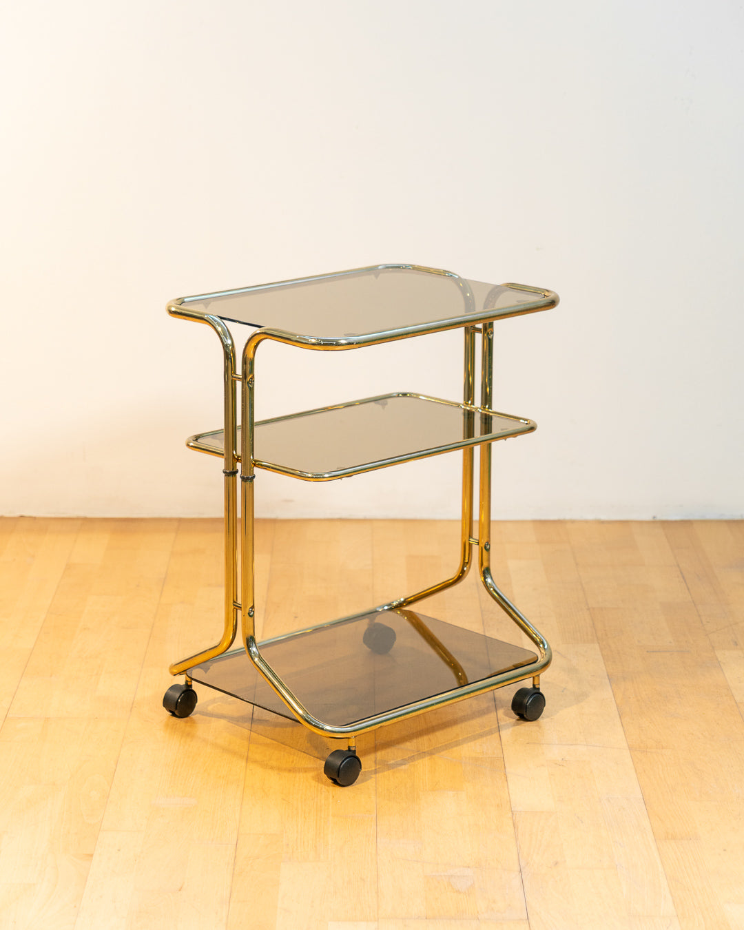 Rare 1970s tubular gold rolling side table with three smoked glass tiers and wheels, vintage Space Age design. Vecino Shop