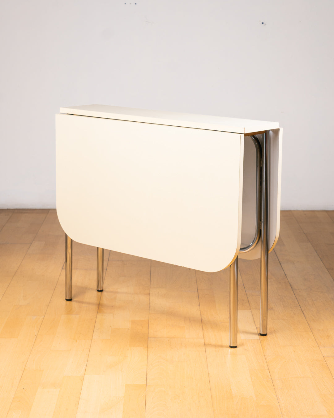 Vintage 1980s folding dining table with off white Formica table top, chrome tubular legs and rounded corners. Space Age space-saving design. Vecino Shop 