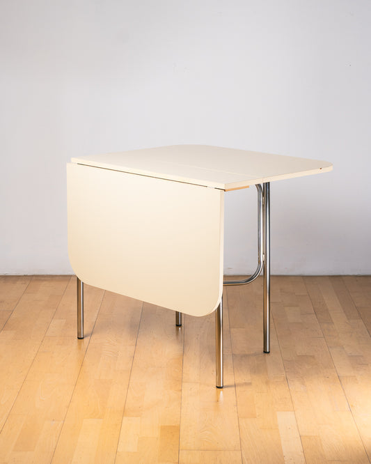 Vintage 1980s folding dining table with off white Formica table top, chrome tubular legs and rounded corners. Space Age space-saving design. Vecino Shop 