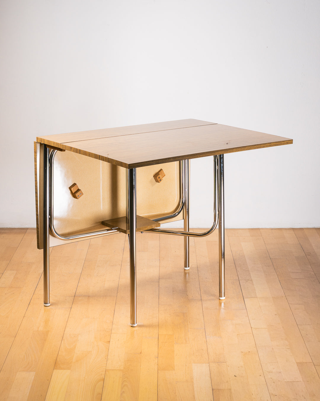 Vintage 1980s folding dining table with brown wood veneer Formica table top, chrome tubular legs and square corners. Space Age space-saving design. Vecino Shop 