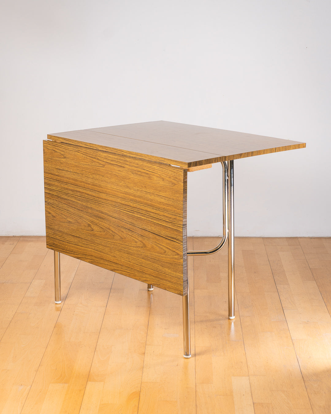 Vintage 1980s folding dining table with brown wood veneer Formica table top, chrome tubular legs and square corners. Space Age space-saving design. Vecino Shop 