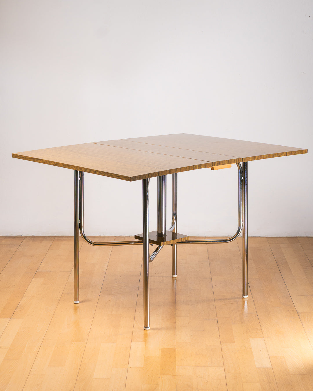 Vintage 1980s folding dining table with brown wood veneer Formica table top, chrome tubular legs and square corners. Space Age space-saving design. Vecino Shop 