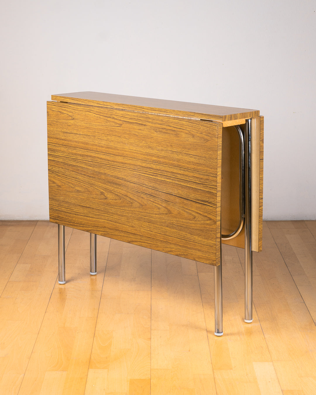 Vintage 1980s folding dining table with brown wood veneer Formica table top, chrome tubular legs and square corners. Space Age space-saving design. Vecino Shop 