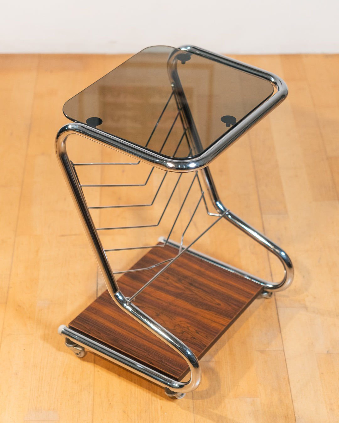 1970s chrome rolling side table with smoked glass top, wooden shelf, wheels, and magazine rack. Vecino Shop