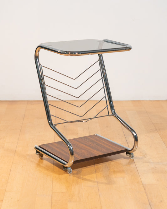 1970s chrome rolling side table with smoked glass top, wooden shelf, wheels, and magazine rack. Vecino Shop
